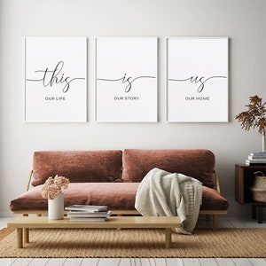 May include: Three white framed prints with black calligraphy. The first print says "this our life", the second print says "is our story", and the third print says "us our home".