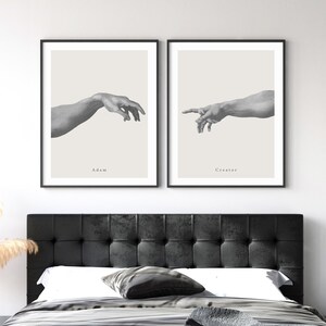 May include: Two black framed prints of the famous Michelangelo painting "The Creation of Adam". The prints are side-by-side and show the hands of God and Adam reaching towards each other. The text "Adam" is below the left hand and "Creator" is below the right hand.