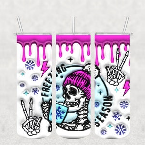 May include: Three white tumblers with a pink dripping design. The center tumbler features a skeleton wearing a pink beanie with a pom-pom and holding a blue cup with a snowflake on it. The text "Freezing Season" is on the tumbler. The left tumbler has a skeleton hand with two fingers up in a peace sign. The right tumbler has a skeleton hand with two fingers up in a peace sign.