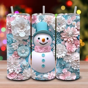 May include: Three insulated tumblers with floral and snowman designs. The tumblers have a light blue background with white, pink, and blue flowers. The central tumbler features a snowman with a blue top hat and pink scarf. Each tumbler has a straw.