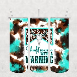May include: Three stainless steel tumblers with lids and straws. The tumblers are wrapped in a brown and turquoise tie-dye pattern. The center tumbler has a cow skull graphic and the text "Should've come with a warning".