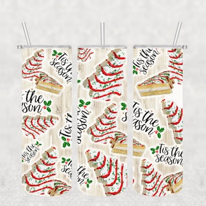 May include: Three white tumblers with a woodgrain background and a repeating pattern of Christmas trees made of cake slices with red and green frosting and the text "Tis the season".