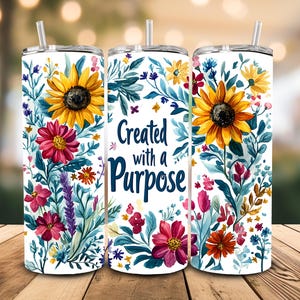 Peut inclure: Un gobelet blanc avec un motif floral composé de tournesols, de fleurs roses, rouges et bleues. Le texte "Created with a Purpose" est imprimé sur le gobelet.