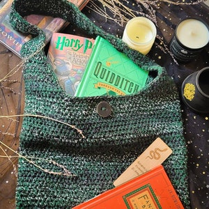 May include: A green and white crocheted shoulder bag with a button closure, holding books with titles like "Harry Potter" and "Fantastic Beasts." A wooden bookmark with a snake design is visible. The bag is filled with books.