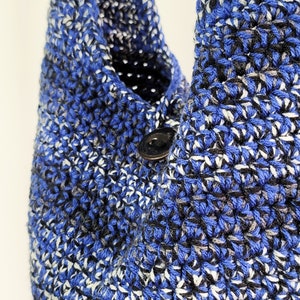 May include: Close-up of a handmade crochet bag in shades of blue, black, and white. The bag features a button closure and a textured stitch pattern. The bag is a shoulder bag style.