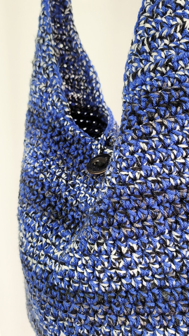 May include: Close-up of a handmade crochet bag in shades of blue, black, and white. The bag features a button closure and a textured stitch pattern. The bag is a shoulder bag style.