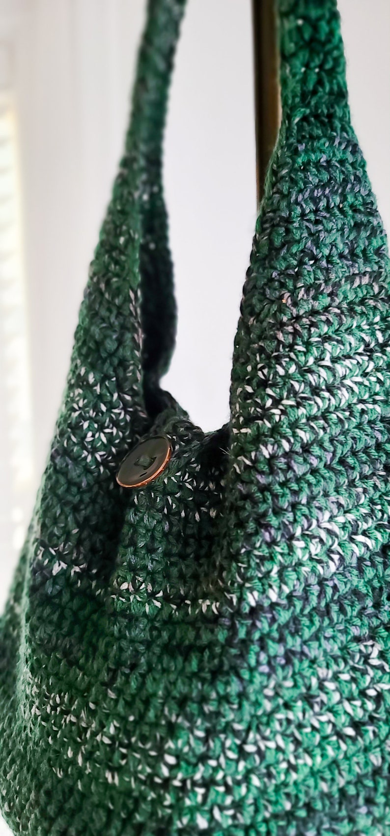 May include: A handmade crochet bag in shades of green, white, and black. The bag features a button closure and a textured stitch pattern. The bag's strap is visible, and the overall design is casual and stylish.