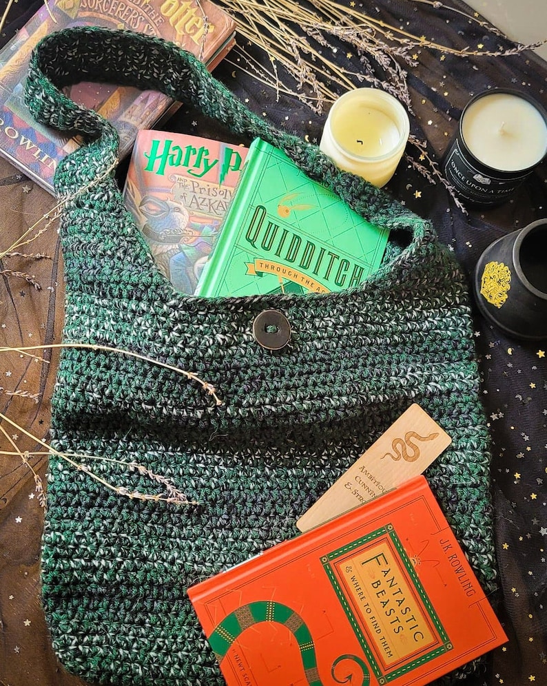 May include: A green and white crocheted shoulder bag with a button closure, holding books with titles like "Harry Potter" and "Fantastic Beasts." A wooden bookmark with a snake design is visible. The bag is filled with books.