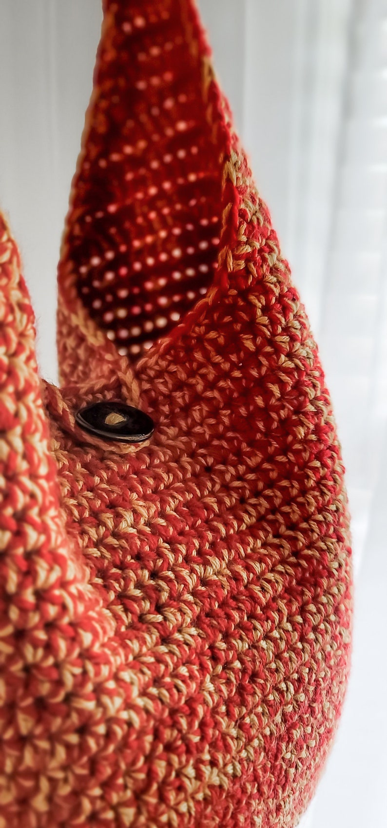 May include: Close-up of a handmade crochet bag in shades of red and tan. The bag features a button closure and a textured, open weave design. The bag is likely made of cotton or a similar yarn.