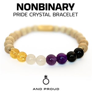 May include: Nonbinary Pride Crystal Bracelet with yellow, white, purple, and black beads. The bracelet has a gold clasp and is made with natural stones. The text "And Proud" is displayed below the bracelet.
