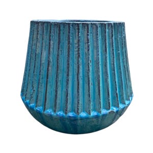Könnte beinhalten: Eine türkisfarbene Keramikvase mit geripptem Design. Die Vase hat einen breiten Boden, der sich nach oben verjüngt, mit vertikalen Rillen, die von oben nach unten verlaufen. Die Farbe ist eine Mischung aus Blautönen mit dunkleren Akzenten in den Rillen.
