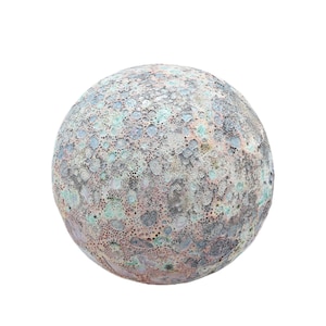 Pode incluir: Objeto decorativo esférico com superfície texturizada. A esfera apresenta um padrão salpicado em tons de cinza, azul e rosa, com uma textura porosa e borbulhante. O objeto está sobre um fundo branco liso.