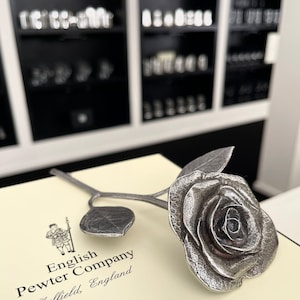 May include: A silver pewter rose with a stem and leaves. The rose is on a white box with the text "English Pewter Company Sheffield, England".