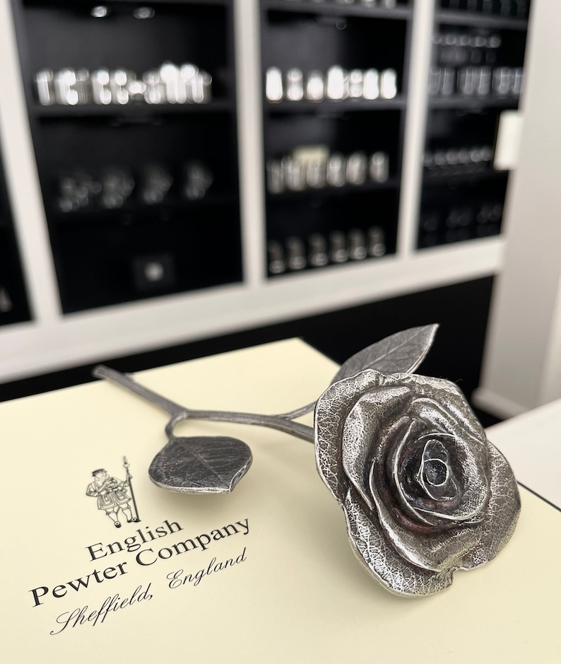 May include: A silver pewter rose with a stem and leaves. The rose is on a white box with the text "English Pewter Company Sheffield, England".