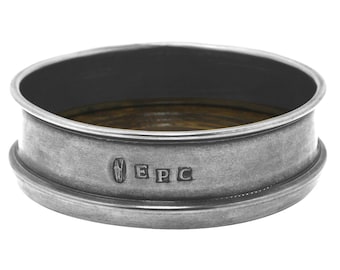 May include: A silver-toned pewter coaster with a wooden insert and the inscription "EPC" on the side.