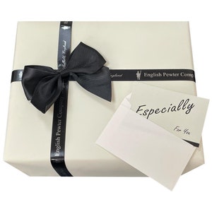 May include: A white gift box with a black satin ribbon tied in a bow. The box is wrapped in white paper with a black ribbon that says "English Pewter Company Sheffield, England". The box is topped with a white card that says "Especially For You".