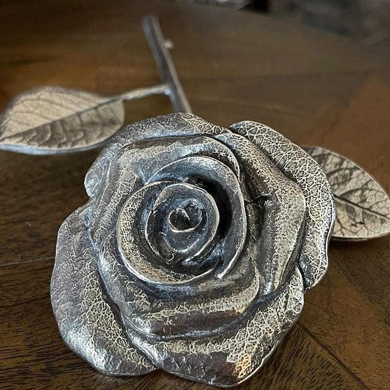 May include: A silver rose with a textured finish, featuring a single rose with leaves. The rose is crafted in a realistic style.