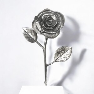 May include: A silver metal rose with two leaves on a stem. The rose is detailed and realistic.