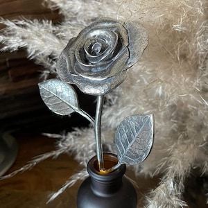 May include: A silver metal rose with leaves in a black vase. The rose is a realistic sculpture with detailed petals and leaves.