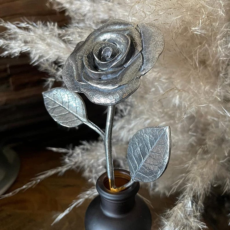 May include: A silver metal rose with leaves in a black vase. The rose is a realistic sculpture with detailed petals and leaves.