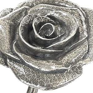 May include: A silver rose sculpture with a textured surface. The rose is in full bloom and has a detailed, realistic design.