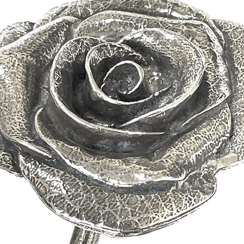 May include: A silver rose sculpture with a textured surface. The rose is in full bloom and has a detailed, realistic design.
