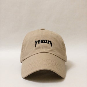 K&ouml;nnte beinhalten: Eine beige Baseballkappe mit einem schwarzen gestickten "YEEZUS"-Logo.