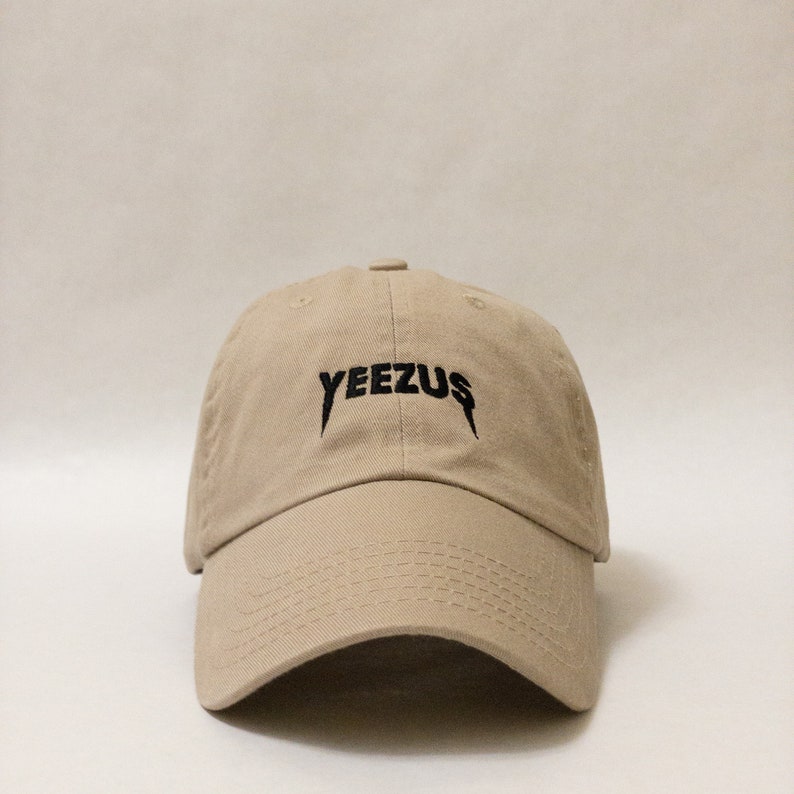 K&ouml;nnte beinhalten: Eine beige Baseballkappe mit einem schwarzen gestickten "YEEZUS"-Logo.