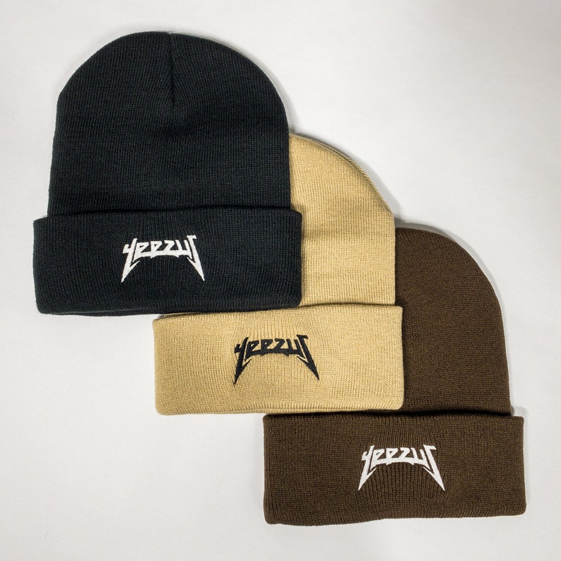 May include: Three beanie hats stacked on top of each other. The top hat is black, the middle hat is beige, and the bottom hat is brown. All three hats have the word "YEEZY" embroidered on the front in white letters.