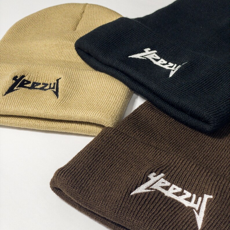 May include: Three knit beanies in different colors: beige, black, and brown. Each beanie has the word "YEEZY" embroidered on the front in white.