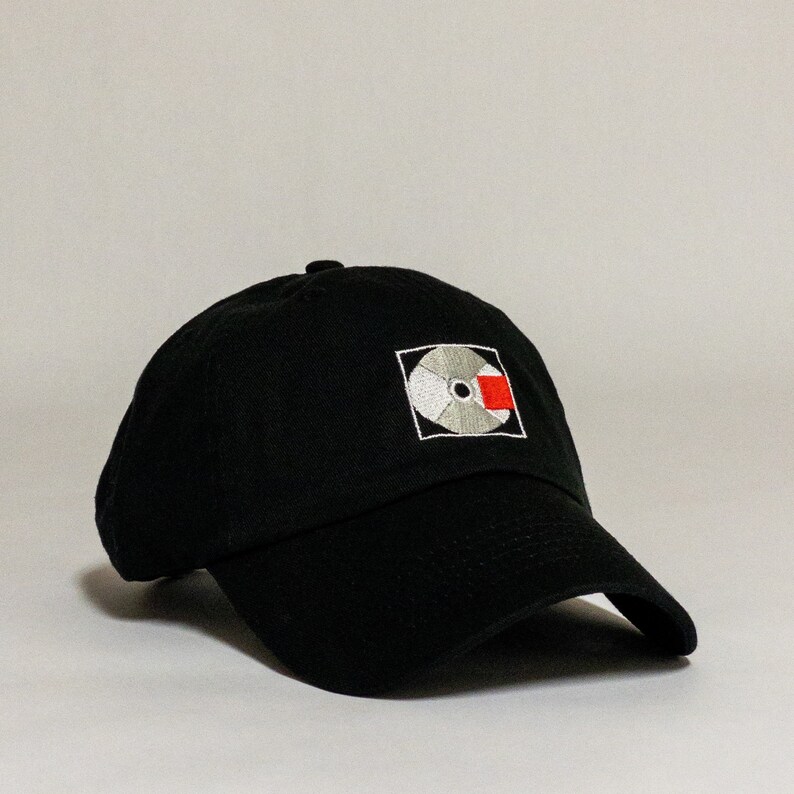 K&ouml;nnte beinhalten: Schwarze Baseballkappe mit einem wei&szlig;en und roten gestickten Logo einer Schallplatte.