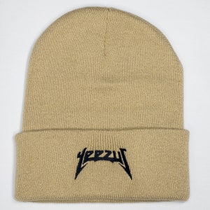 May include: A beige knitted beanie with a black embroidered "YEEZY" logo.