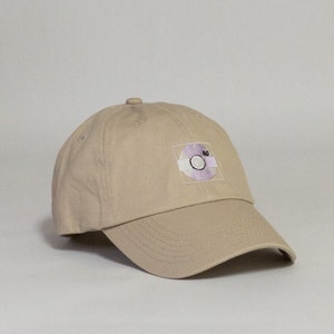 May include: A beige baseball cap with a purple and white embroidered patch of a record with the number 80 on it.