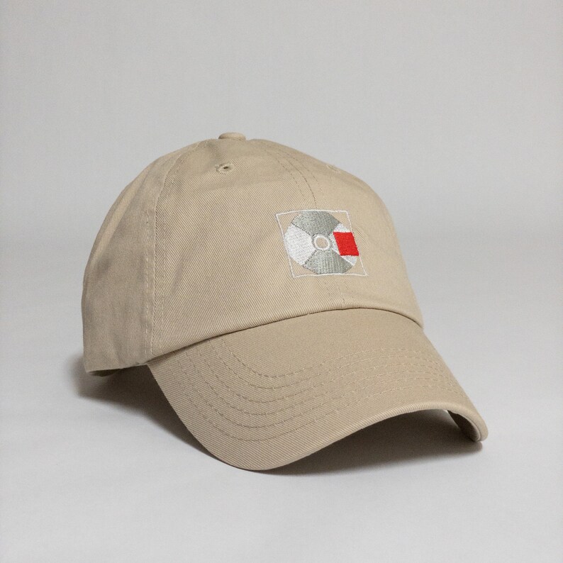 K&ouml;nnte beinhalten: Eine beige Baseballkappe mit einem wei&szlig;en und roten gestickten Schallplatten-Design.
