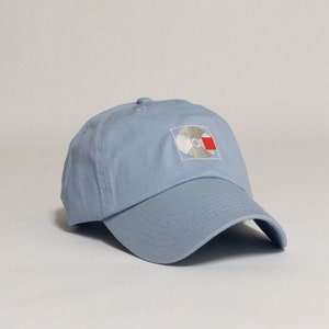 K&ouml;nnte beinhalten: Eine hellblaue Baseballkappe mit einem wei&szlig;en und roten gestickten Logo einer Schallplatte.