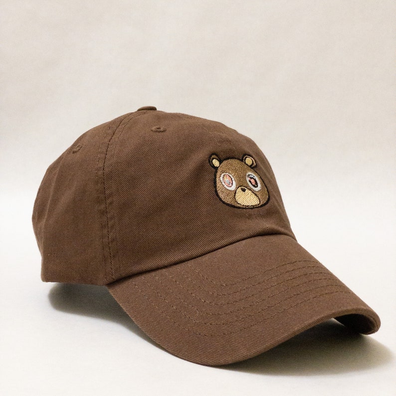 May include: A brown baseball cap with an embroidered brown bear with rainbow eyes.