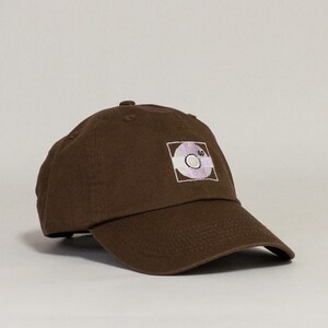 May include: A brown baseball cap with a white and purple embroidered design of a record with the number 80 on it.