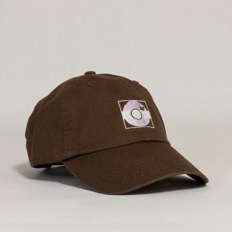 May include: A brown baseball cap with a white and purple embroidered design of a record with the number 80 on it.