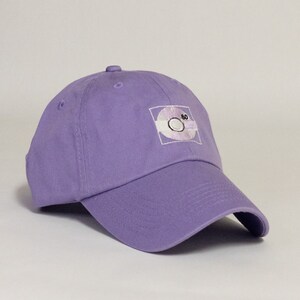 May include: A purple baseball cap with an embroidered white design of a cassette tape with the number 80 on it.