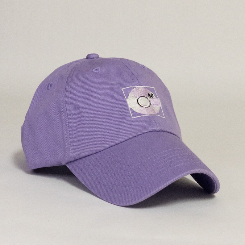 May include: A purple baseball cap with an embroidered white design of a cassette tape with the number 80 on it.