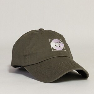 May include: A green baseball cap with an embroidered white and purple design of a record with the number 80 on it.