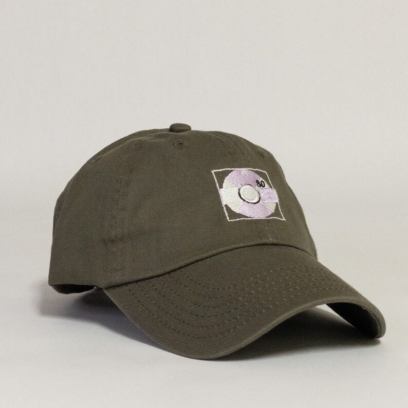 May include: A green baseball cap with an embroidered white and purple design of a record with the number 80 on it.