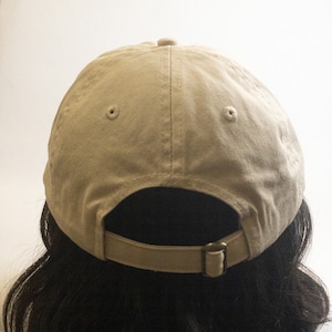 May include: A beige baseball cap with a brown adjustable strap at the back. The cap has two small holes on the top.