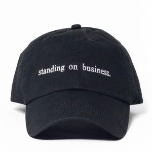 May include: Black baseball cap with the embroidered text "standing on business." The cap has a curved brim and a small button on top. The hat is made of a soft, durable fabric.