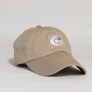 May include: A beige baseball cap with a pink and white embroidered design of a compact disc with the number "80" on it.