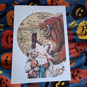 May include: A print featuring characters from a fantasy movie. The artwork depicts a woman in a white blouse, a large furry creature, and other figures. The text "Should you need us" is written in a circular pattern.