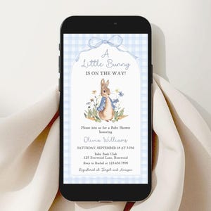 Può includere: Uno smartphone mostra un invito per un baby shower. L'invito presenta un'illustrazione di un coniglietto con una giacca blu, circondato da fiori. Il testo recita "A Little Bunny Is On The Way!" e include i dettagli dell'evento.