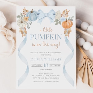 May include: A white baby shower invitation card featuring watercolour illustrations of blue and orange pumpkins, foliage, and a large blue bow at the top. The text reads: a little PUMPKIN is on the way! PLEASE JOIN US FOR A BABY SHOWER HONOURING OLIVIA WILLIAMS OCTOBER 18 SATURDAY 5:00-8:00 PM BABY BASH CLUB 125 EVERWOOD LANE, ROSEWOOD RSVP TO RACHEL AT 123.456.7890 REGISTERED AT TARGET AND AMAZON.