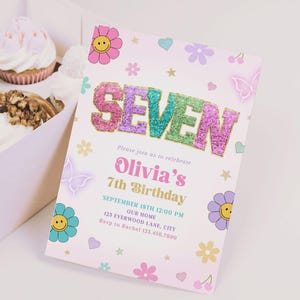 May include: A light pink birthday invitation with the word "SEVEN" in glitter letters. The invitation includes the text "Olivia's 7th Birthday" and floral and butterfly illustrations. Cupcakes are in a box in the background.