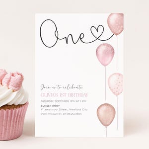 以下が含まれることがあります： 白いフロスティングのピンク色のカップケーキが、誕生日の招待状の隣にあります。招待状にはハート付きの「One」とピンク色の風船が描かれています。テキストは、オリビアの1歳の誕生日パーティーへのゲストを招待しています。